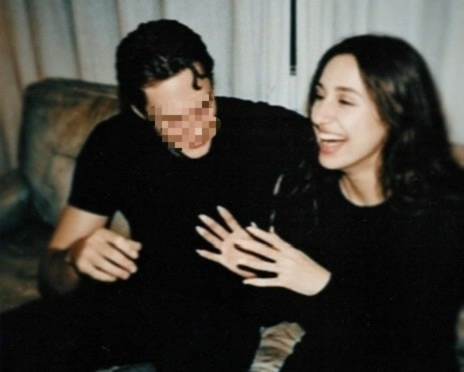 Aylin Baykal laughing while seated beside Bill Gaard whose face is obscured in a casual indoor photograph.
