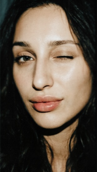 Close-up portrait of Aylin Baykal resting her face against one hand and looking into the camera.