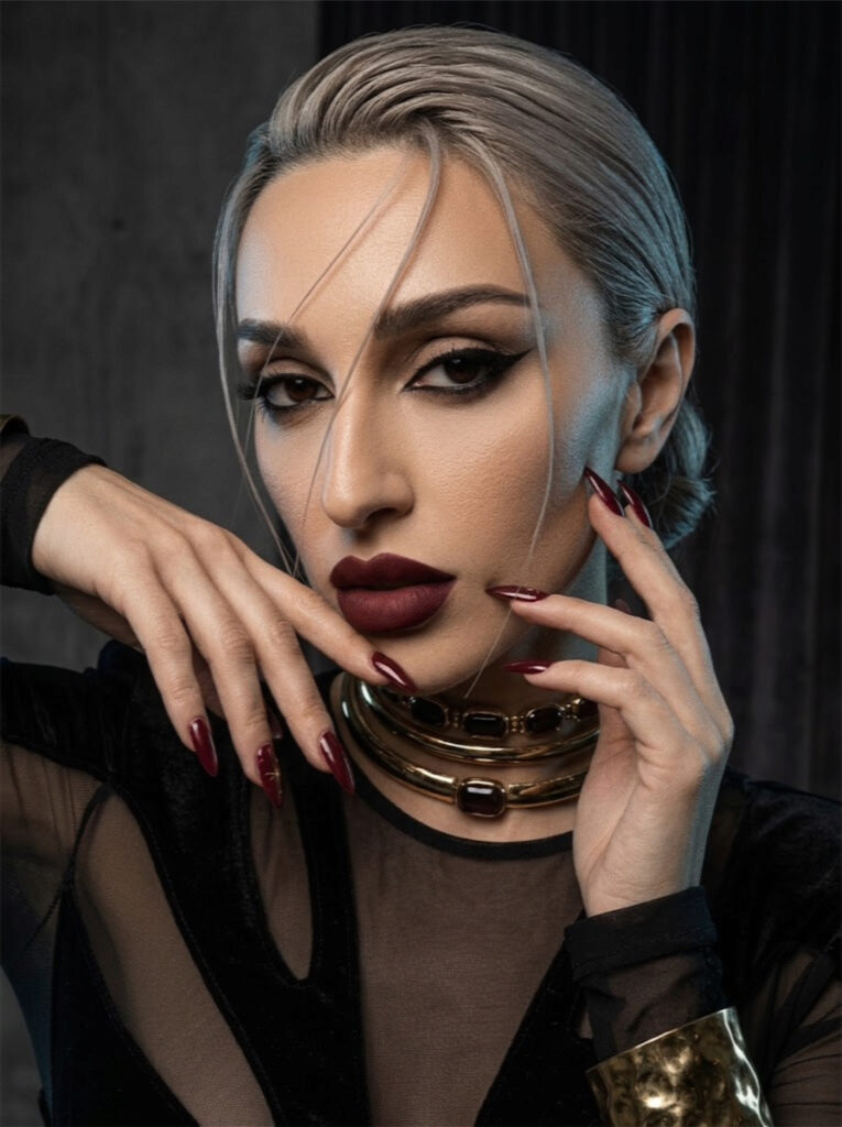 Portrait of Aylin Baykal wearing two gold Starchuska necklaces and a hammered cuff over a black sheer bodysuit.
