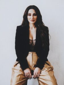Aylin Baykal seated in a black blazer, lace bodysuit and gold wide-leg trousers for Starchuska Women’s AW’26.