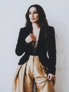 Aylin Baykal standing in a black blazer, lace bodysuit and gold trousers for Starchuska Women’s AW’26.