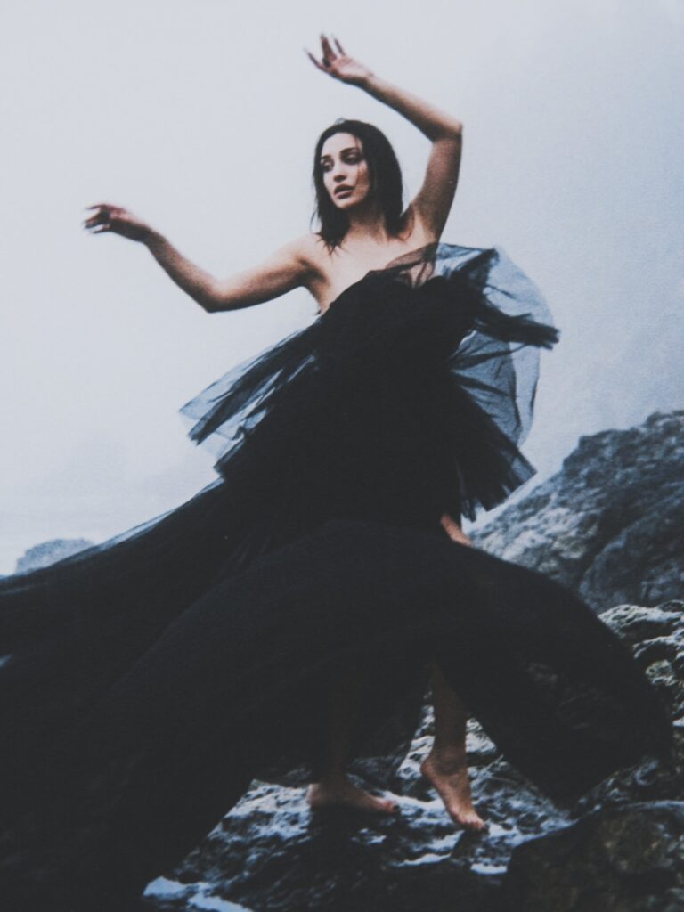 Aylin Baykal barefoot in a dramatic black tulle gown on a rocky shoreline for Starchuska Women’s AW’26.