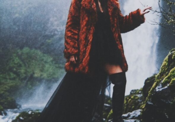Aylin Baykal in a rust faux-fur coat and black dress beside a misty waterfall for Starchuska Women’s AW’26.