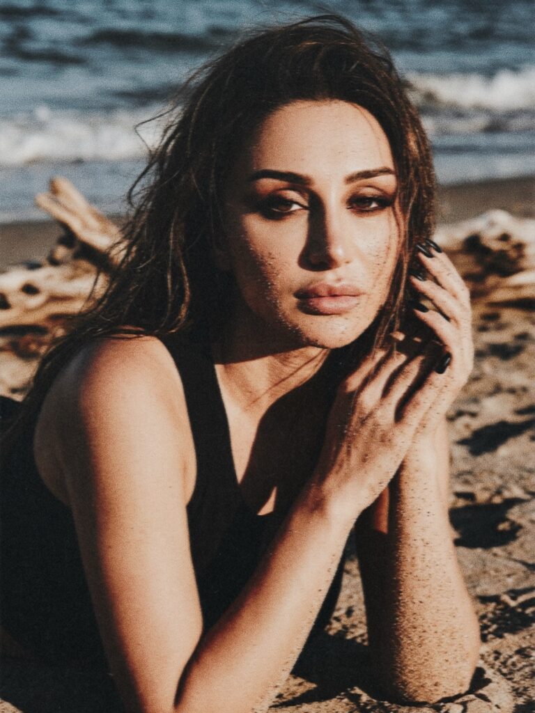 Aylin Baykal seated on the Oregon coast wearing a cream shearling coat for Starchuska Women’s AW’26.